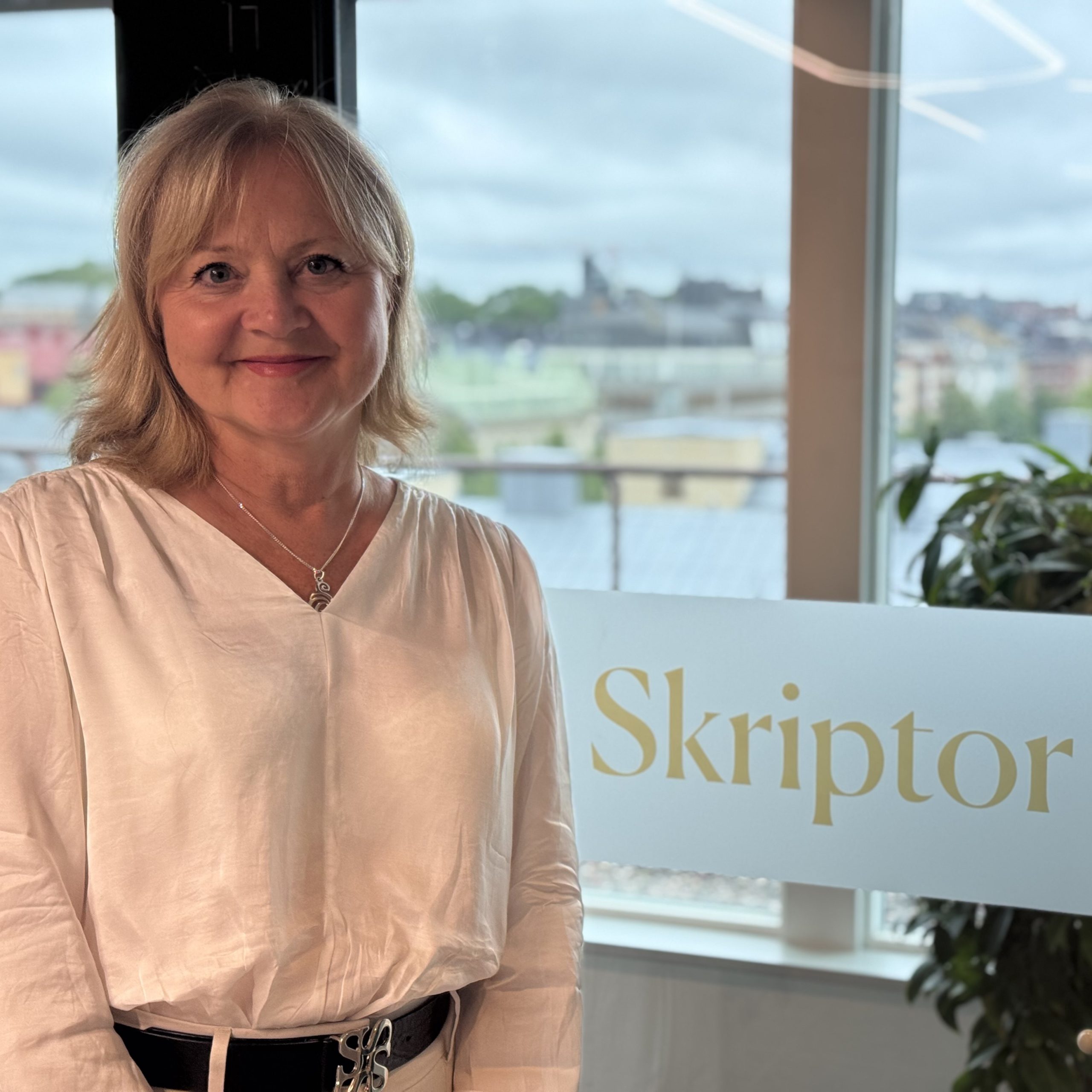 Person står framför ett fönster med utsikt över en stad och en skylt med texten Skriptor.